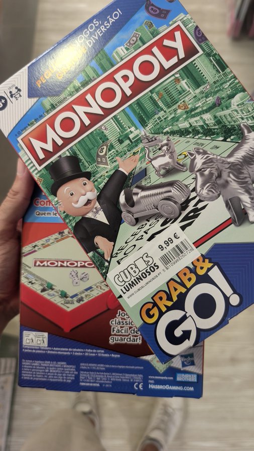 A hand holding two Monopoly board game boxes with Portuguese text including 'JOGOS DIVERSÃO!' and '9,99 €', along with a 'GRAB & GO!' sign.