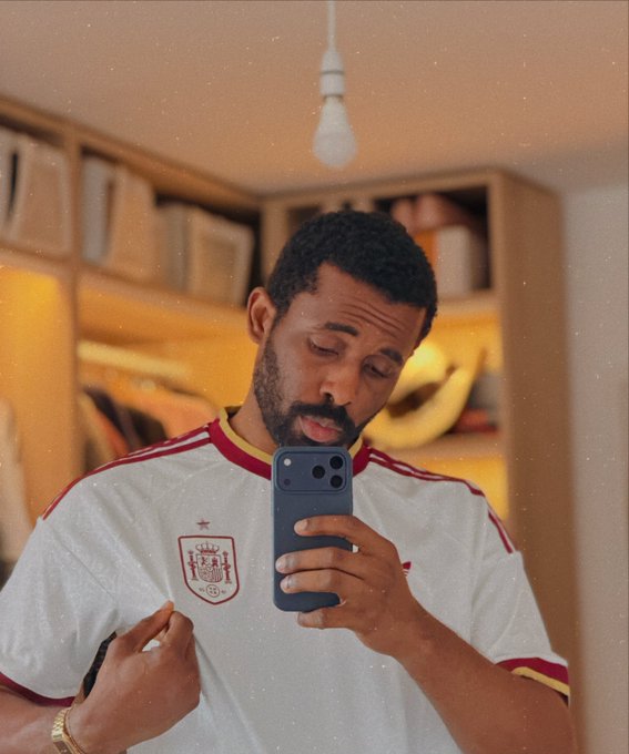 A man takes a mirror selfie in a walk-in closet, wearing a white and red soccer jersey with a crest featuring stars and a castle, paired with a gold watch. The image ties to "The Transformation" by showing a stylish, confident self-reflection moment, suggesting personal growth through fashion and self-presentation.