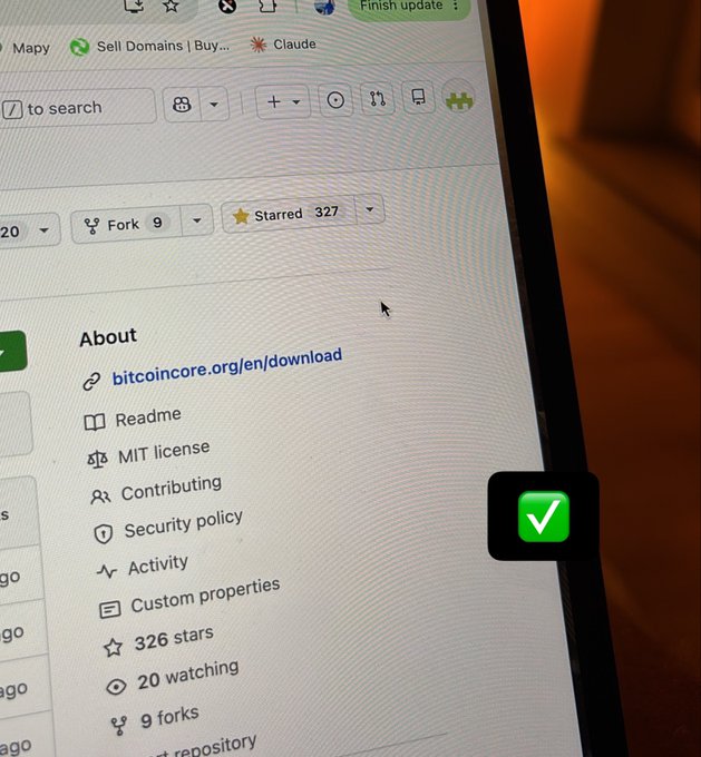 A close-up photo of a computer screen displaying the Bitcoin Core GitHub repository page (bitcoincore.org/en/download), showing 326 stars, 20 watching, and 9 forks, with a green checkmark sticker visible on the monitor.