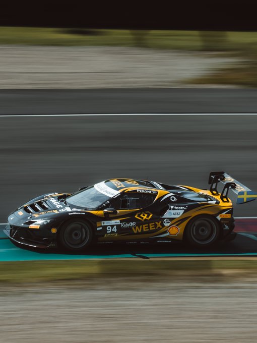 A black and yellow race car, number 94, with WEEX and Shell sponsorship logos, speeding along a track with motion blur.