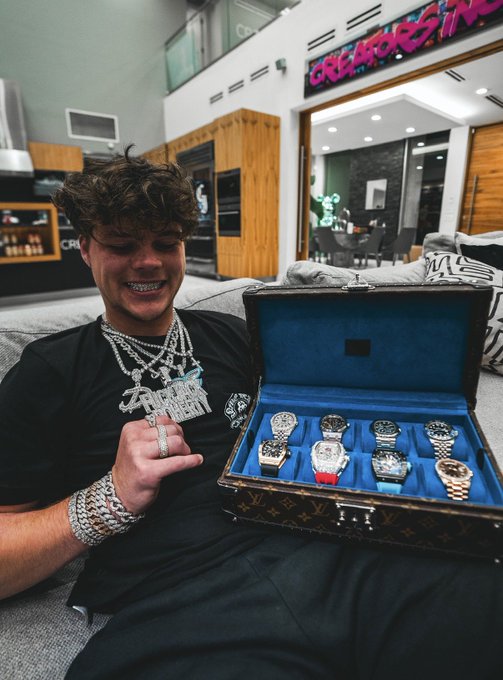 A young man with braces and flashy jewelry smiles while displaying a Louis Vuitton case filled with multiple luxury watches, showcasing his new "Black Bull" timepieces.