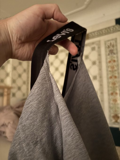 A hand holds up a pair of grey Calvin Klein underwear by the waistband, revealing the brand name printed on the inside.