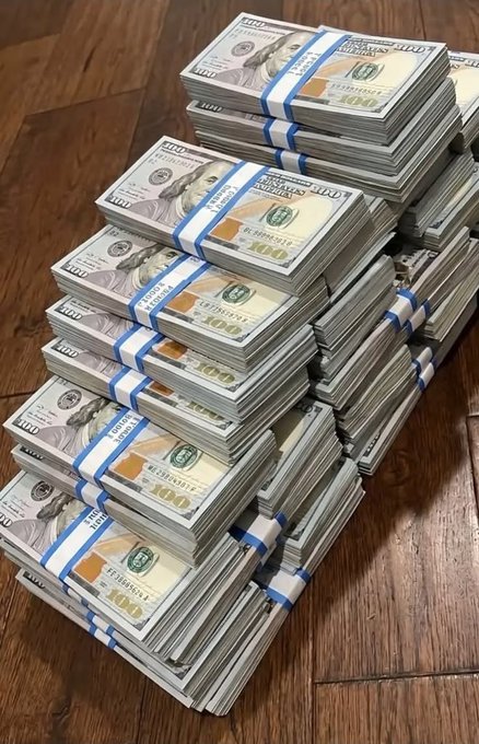 A photo of numerous stacks of US $100 bills bound with straps piled on a wooden floor.