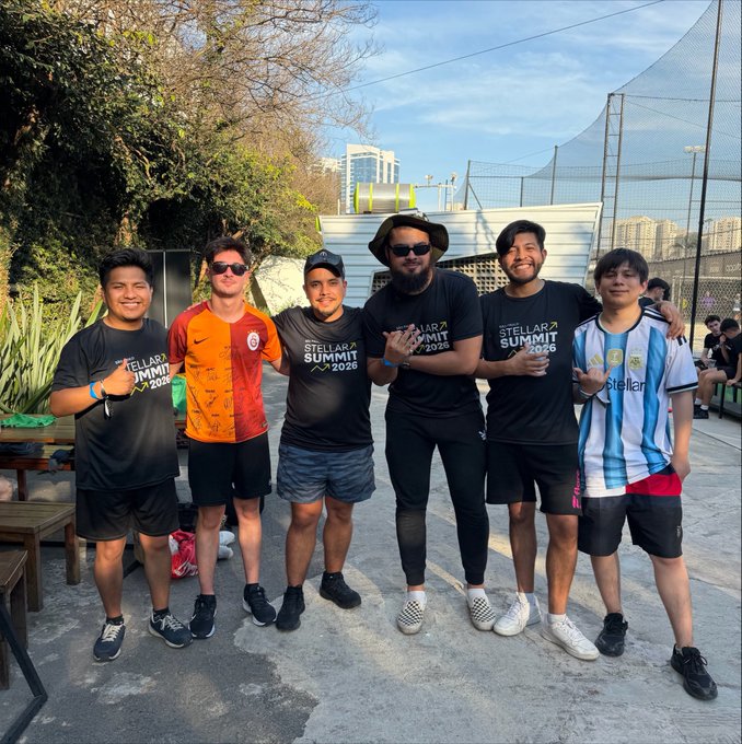 Group photo of seven smiling men posing together outdoors, several wearing black 'STELLAR SUMMIT 2026' t-shirts, with one in a red/black jersey and another in an Argentina soccer jersey.