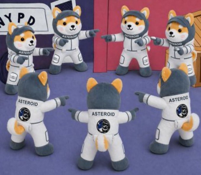 A group of plush mascot toys dressed as astronauts with 'ASTEROID' written on their suits, arranged in a circle pointing at each other.
