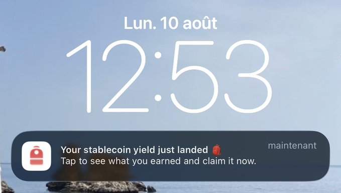An iPhone lock screen showing the date 'Lun. 10 août' (Monday, August 10) at 12:53, with a notification from a finance app stating 'Your stablecoin yield just landed - Tap to see what you earned and claim it now.'