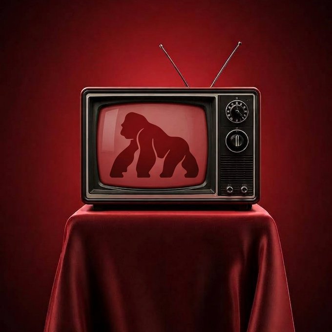 A vintage television with two antennae sits on a red-cloth-covered table against a deep red backdrop, displaying a dark red silhouette of a gorilla on its screen.