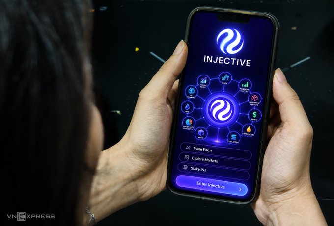 A person holds a smartphone displaying the Injective cryptocurrency app interface, featuring a blue glow, various feature icons, and options to 'Trade Perps', 'Explore Markets', and 'Stake INJ', with a VNExpress watermark.