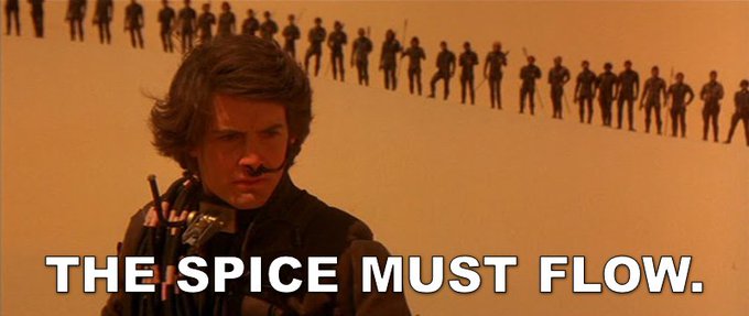 A young man with long hair stands in a desert landscape with a long line of figures in the background, accompanied by the bold text "THE SPICE MUST FLOW." The image references the famous dune scene from *Dune*, drawing a parallel to the relentless, ongoing flow of cryptocurrency mining—suggesting that even as the algorithm shifts from SHA256 to BLAKE2b, the mining process keeps moving forward.