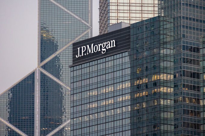 The J.P. Morgan logo is displayed prominently on a modern glass skyscraper, symbolizing the bank's dominant presence in the evolving financial landscape. The image reinforces the post's message about major banking institutions positioning themselves as the foundational infrastructure in the emerging stablecoin race.