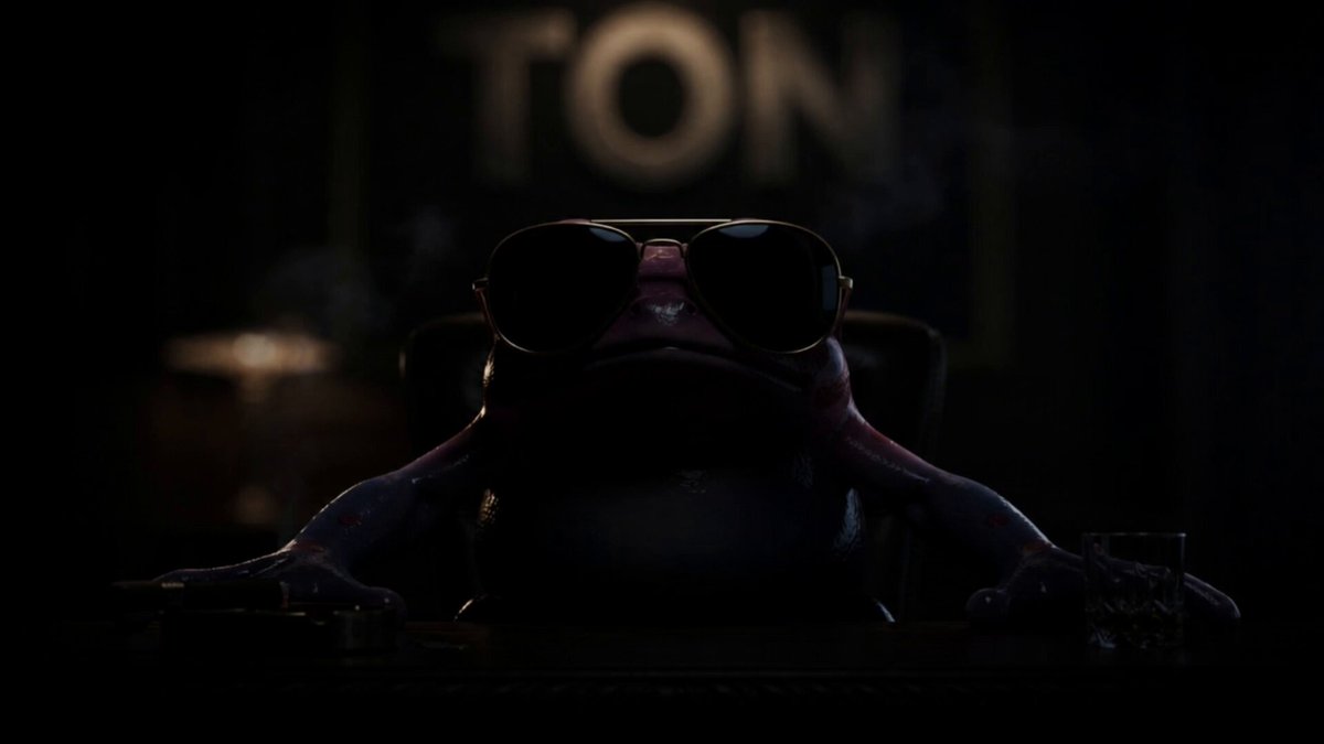 The image features a cartoon frog wearing sunglasses, sitting at a desk with a computer monitor behind him. The background shows a dark room with a neon sign that reads "TON" above the frog's head. There are also two glasses on the desk in front of the frog and a keyboard nearby. The post about this meme content is titled "I’ve seen a lot of meme contents on Ton But nothing prepared me for this Tbh the community outdid themselves absolute cinema".