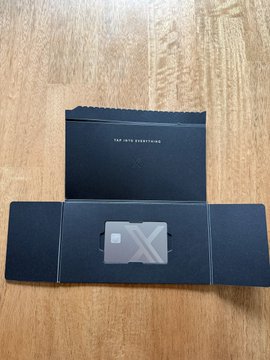 A black card holder sits open on a wooden floor, revealing a black card with 'X' branding inside.