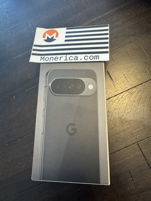 A Google Pixel smartphone box with a Monerica.com business card rests on a dark wooden surface.