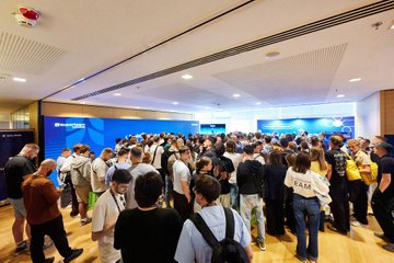 The image shows a large group of people gathered together, possibly attending an event or conference. The attendees are standing around each other, engaged in conversations and interactions. There are at least 13 visible individuals in the scene, with some wearing backpacks. A prominent feature is a blue banner hanging prominently from the ceiling, which appears to be part of the event's decor.

The post that accompanies this image is titled "50+ hackers building mobile apps for @solanamobile with @TryNoahAI Happy to have supported builders on the ground!". The post seems to be promoting an app development competition or a similar event related to mobile app development and hacking activities.