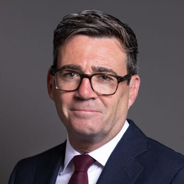 A portrait photograph of Andy Burnham, a middle-aged man with short dark hair wearing glasses, a dark suit, white shirt, and burgundy tie against a gray background. The image accompanies a post announcing him as the UK's next prime minister, noting his crypto-friendly stance and support for making Manchester a "Web3 powerhouse."