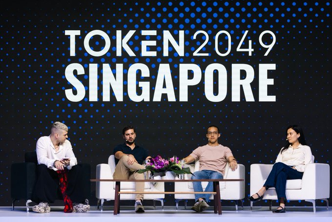 A panel discussion at TOKEN 2049 SINGAPORE features four speakers seated on white chairs on stage with a large branded backdrop.
