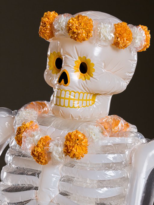 An inflatable skeleton figure decorated with orange and white marigold flowers, characteristic of Day of the Dead (Día de los Muertos) decorations.