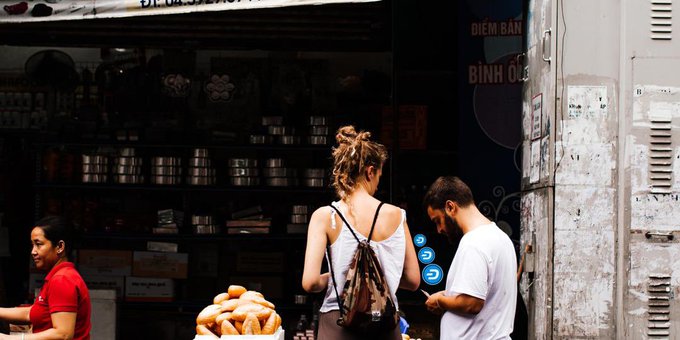 A street scene outside a Vietnamese shop displaying metal cookware, with people gathered at the entrance; visible text includes 'ĐIỂM BÁN BÌNH Ủ' on the storefront.