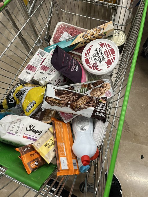 A grocery shopping cart filled with items including a pack of ground beef, a tub of "Tereyağı Tereyağı" (butter), a "Nesquik" cereal bar package, "Sleepy" baby diapers, cheese, and milk. The post invites guesses on the total cost in Turkish lira (₺), with a TRC-20 wallet address prize for the correct guesser.