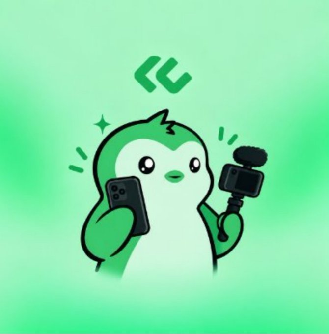 A cute cartoon green penguin mascot holding a smartphone in one hand and a small camera in the other, with a green chevron logo above its head against a light green background.