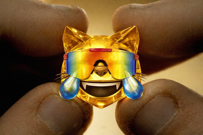 A pair of hands holds a small, translucent yellow crystalline cat figurine wearing rainbow-colored sunglasses, with a speech bubble graphic.