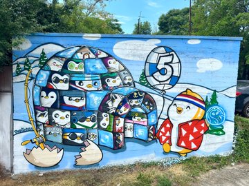 A vibrant outdoor mural featuring a large igloo made of cartoon characters, a penguin character, and a prominent number '5' painted on a wall.