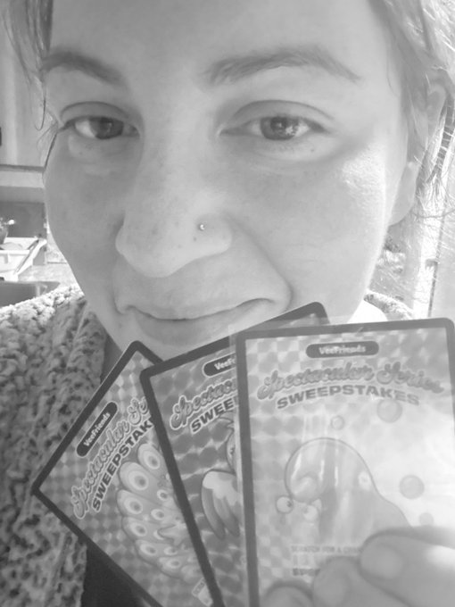 A black-and-white close-up selfie of a person holding three VoF Friends Spectacular Series Sweepstakes cards in front of their face.