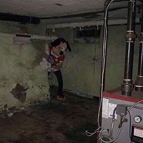 A creepy Mickey Mouse doll hangs from pipes in a dimly lit, moldy basement next to a furnace, creating an unsettling scene that matches the eerie, ominous tone of the post jokingly inviting visitors to a secretive "2026 ETH bull meetup."