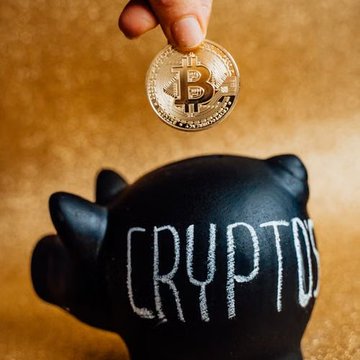 A person drops a gold Bitcoin coin into a black piggy bank labeled "CRYPTO," symbolizing the growing accumulation of BTC by mid-tier wallets, which have added over 113,950 BTC since mid-July to hold approximately 5.24 million BTC.