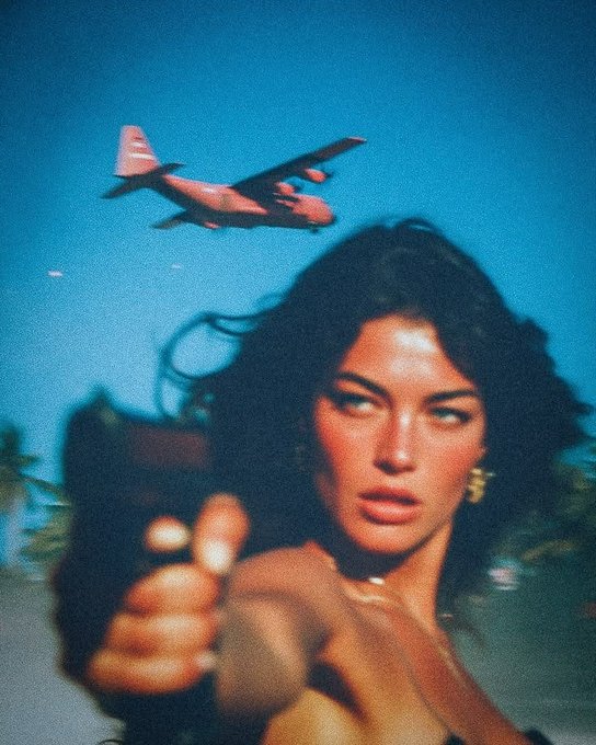 A stylized photo of a woman with dark hair aiming a gun at the camera, with a vintage propeller airplane flying in the teal sky behind her.