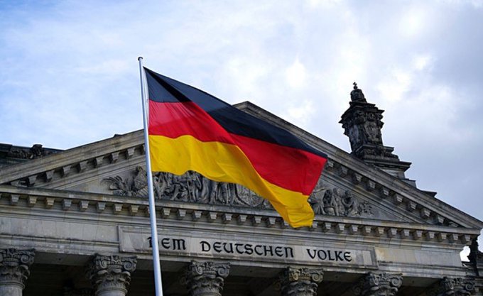 A German national flag flies proudly in front of the Reichstag building, prominently displaying the inscription "DEM DEUTSCHEN VOLKE" (To the German People), symbolizing Germany's commitment to digital innovation as Deutsche Bank, the country's largest bank, announces its entry into Bitcoin custody services for institutional clients.