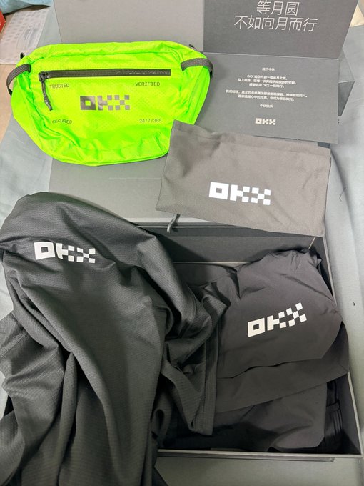 An unboxed OKX branded promotional package containing a neon green waist bag, a gray t-shirt, and a gray pouch.