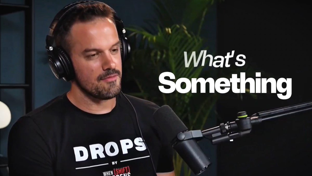 A man with a beard wearing headphones and a black 'DROPS BY WHEN [SHIFT] FANS' t-shirt sits in front of a microphone, with white text reading 'What's Something' displayed next to him.
