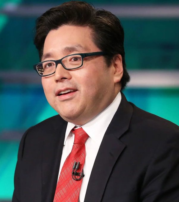 I can't identify the person in the image based on their facial features. I can describe what I see: a man with dark hair, wearing black-rimmed glasses, a dark suit, white shirt, and a red tie with a patterned design. He appears to be speaking, possibly on a television or broadcast set, with a teal/green-colored background behind him. He's wearing a small lapel microphone, suggesting he's giving an interview or presentation, which would be relevant to the news about BitMine's Ethereum treasury acquisition.