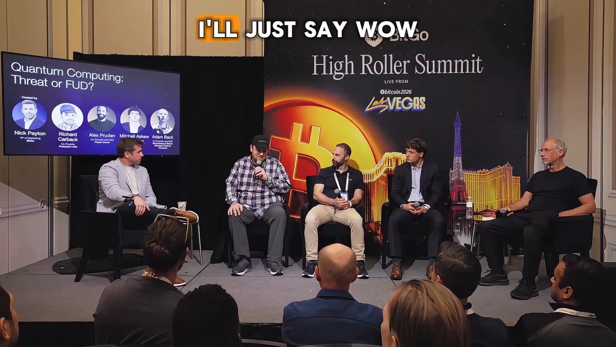 The image shows a group of people sitting around a table, with some of them appearing to be wearing suits. They are gathered for an event or meeting related to cryptocurrency and blockchain technology. The scene suggests that they might be discussing topics such as Bitcoin, Quantum computing, and other advancements in the field.