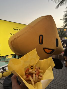 A hand holding a yellow box of fries topped with sauce, in front of an inflatable brown star-shaped mascot near a sign for CubeNC.