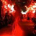 A dimly lit scene of a woman in a flowing dress walking through a corridor illuminated by red lanterns.