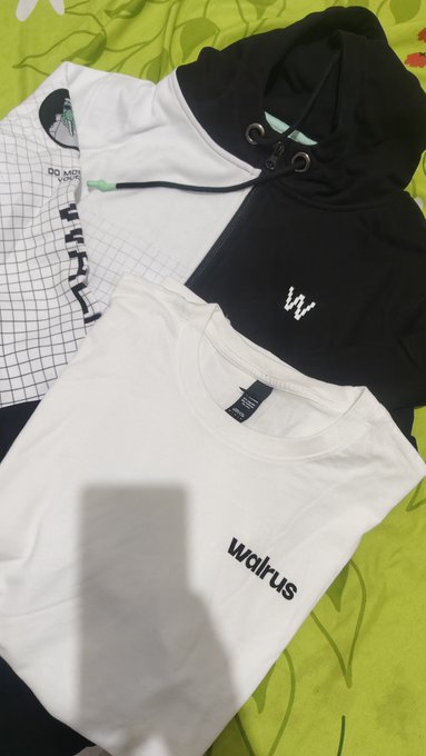 Clothing items laid out on a green sheet, including a white 'walrus' t-shirt, a black hoodie with a 'W' logo, and other folded apparel.