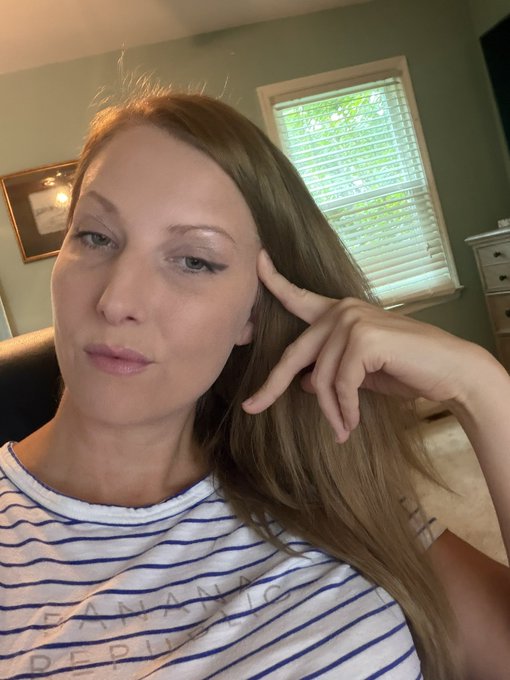 A woman in a striped t-shirt poses for a selfie in a room with a window and dresser, holding her hand up near her face. The shirt appears to display text including the letters "ANAG" and "DEL," fitting the casual "goodnight friends" vibe of the post.