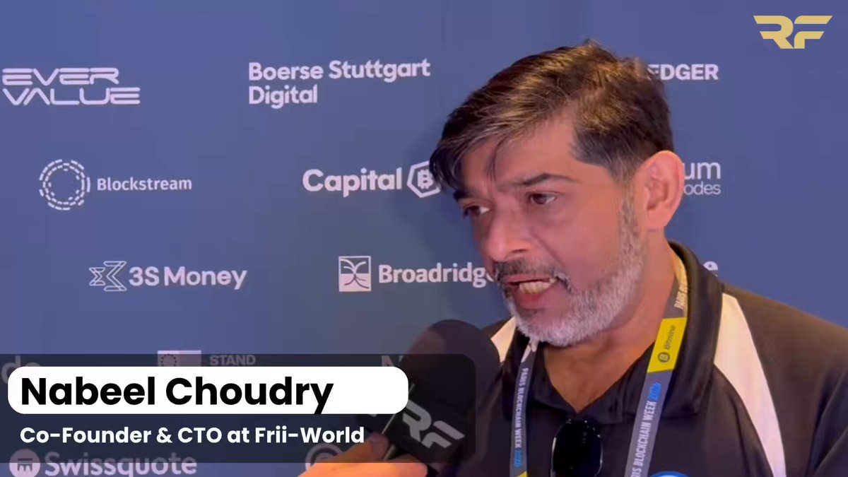 The image features a man wearing a black shirt, speaking into a microphone during an interview or press conference. The background of the image shows a blue wall with various logos and text written on it. One of the logos reads "XRP Family". This suggests that the man might be discussing the impact of cryptocurrency or blockchain technology in relation to traditional payment methods.