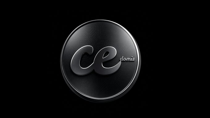 A sleek circular black badge with metallic silver trim displays the stylized "ce" logo alongside the "domis" text, representing the Cedomis brand against a dark background. The image visually reinforces the launch announcement by showcasing the project's polished emblem to mark the official debut of the $CEDO token.