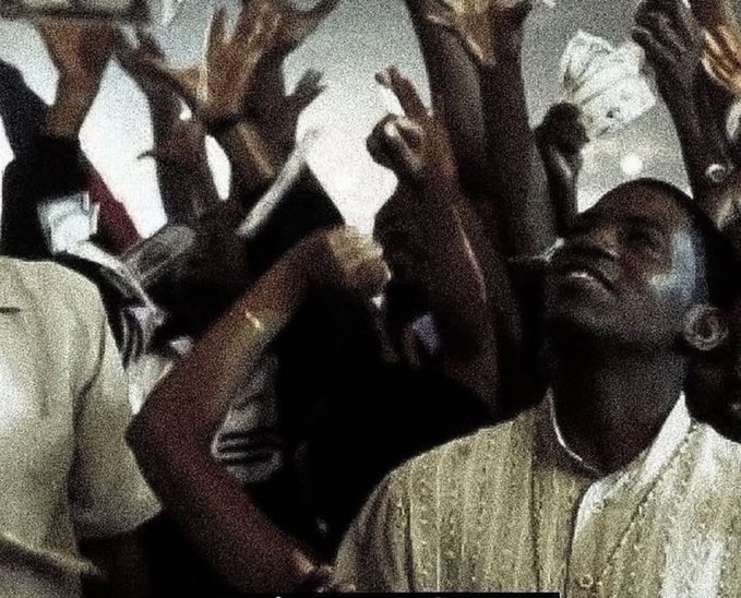 A close-up shot of a crowd with many hands raised, featuring a young Black person with their face tilted upward and eyes closed in an emotional expression.