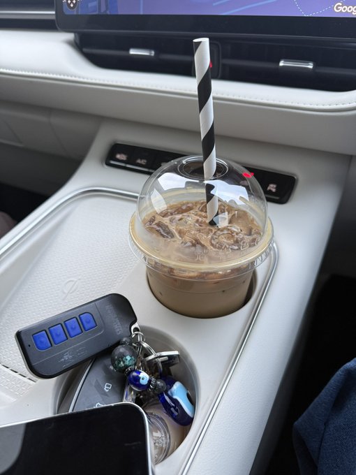 An iced coffee with a striped straw sits in a car cup holder next to a car key fob and a smartphone, with a Google display visible on the dashboard. The image complements the post's "Rise & Shine CT!" message by showing the free coffee being offered to Solana wallet holders.