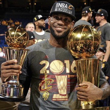 LeBron James, wearing a "2016 NBA Champions" shirt and "NBA Champions" cap, proudly holds the Larry O'Brien Championship Trophy and Finals MVP trophy after leading the Cleveland Cavaliers to their historic NBA title—visual context for the Polymarket betting odds showing Cleveland as heavy favorites to sign him.