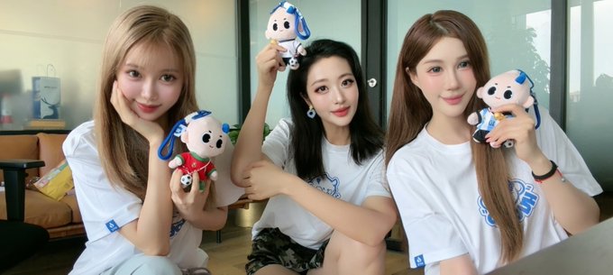 Three young women in matching white t-shirts posing together while holding small plush dog mascots.