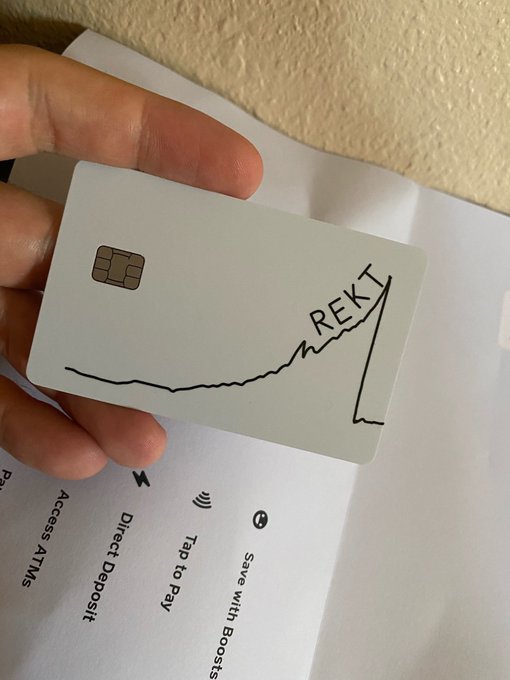 A hand holding a metal bank card with a hand-drawn line graph showing a sharp upward spike labeled "REKT," positioned over an instruction sheet mentioning "Direct Deposit," "Tap to Pay," and "Save with Boosts."