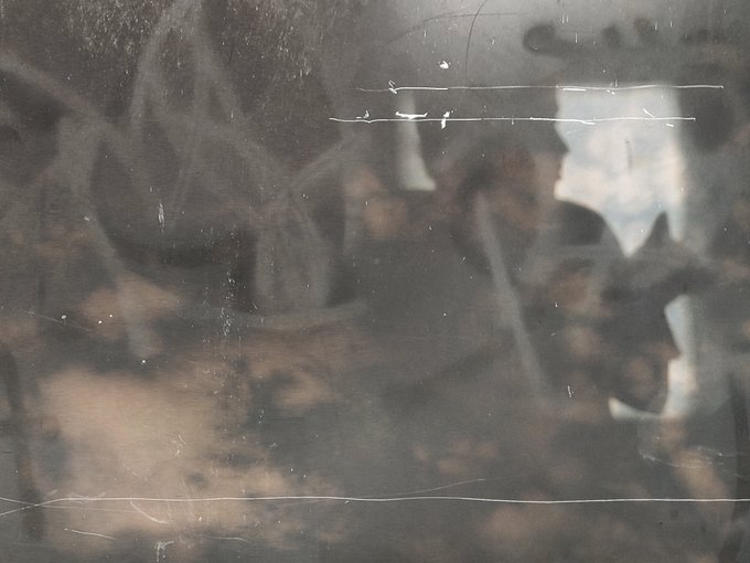 A close-up of a dirty, textured surface with scratches and worn markings, possibly a wall or panel, showing vague dark and light shapes.