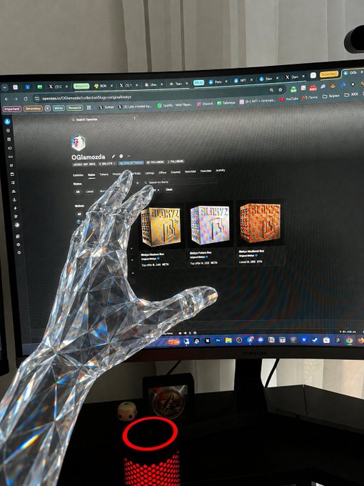 A translucent crystal-like hand sculpture reaches toward a computer monitor displaying the OGdiamonds website for "Original Blokyz" with prices starting at $25. The artwork visually reinforces the post by embodying the feel and brilliance of the crystal-themed Blokyz NFT collection.