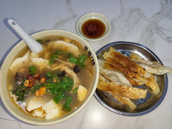 A meal of Chinese soup with tofu, egg, and cilantro, served alongside a plate of pan-fried dumplings (gyoza) and a small dish of dipping sauce.