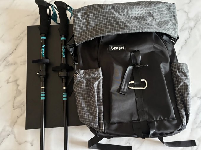 A black Bitget-branded backpack and matching trekking poles are laid out on a marble surface.